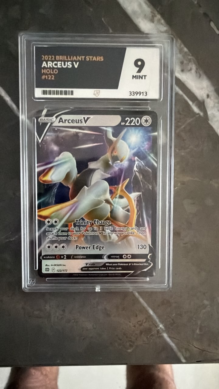 A graded Pokémon TCG card, Arceus V Holo #132 from the 2022 Brilliant Stars set, sealed in a clear PSA-style holder and photographed on a dark marble-like surface.