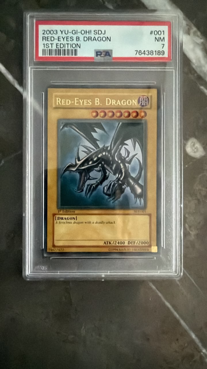 A graded Yu-Gi-Oh! trading card of Red-Eyes B. Dragon, PSA 7, sealed in a clear plastic protective slab on a dark marble surface.