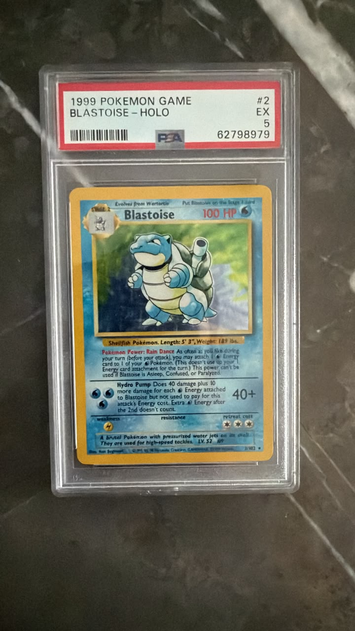 A graded 1999 holographic Blastoise Pokémon trading card inside a PSA slab, photographed on a dark marble-like surface.