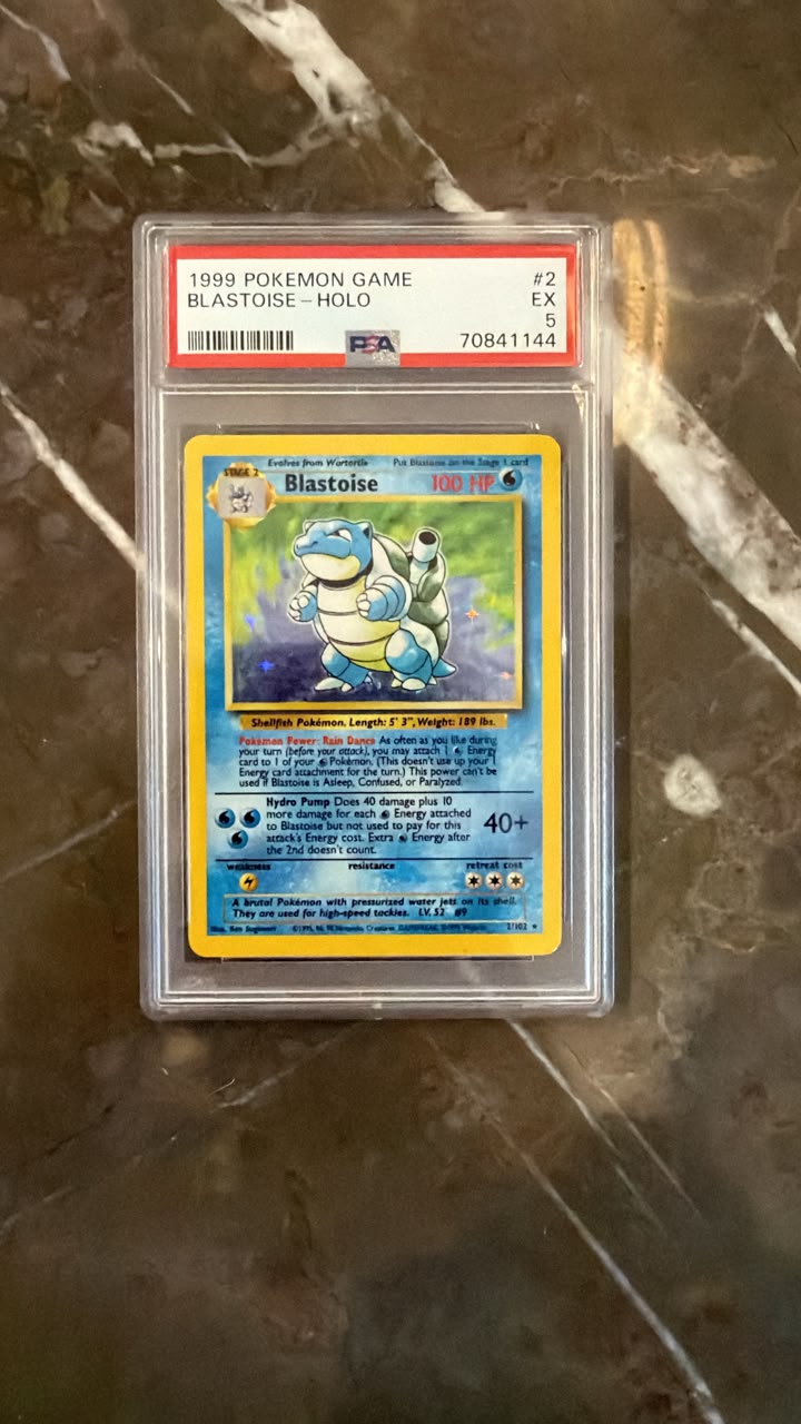 A graded 1999 Pokémon Blastoise trading card, PSA 8, sealed in a protective plastic holder and placed on a dark marble surface.
