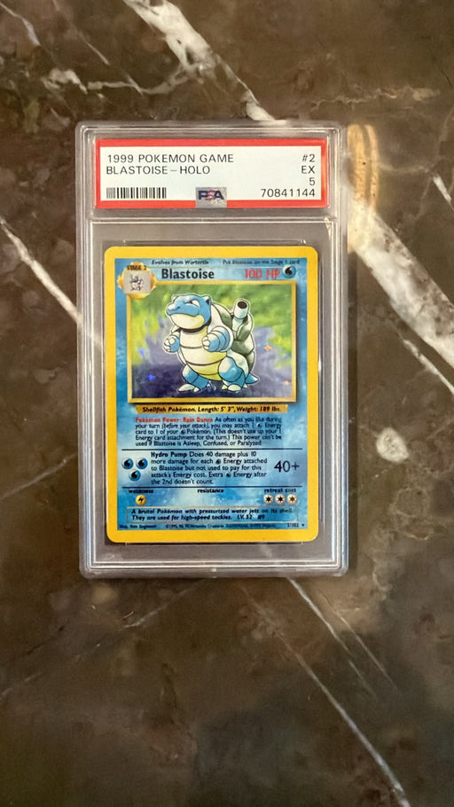 A graded 1999 Pokémon Blastoise trading card, PSA 8, sealed in a protective plastic holder and placed on a dark marble surface.