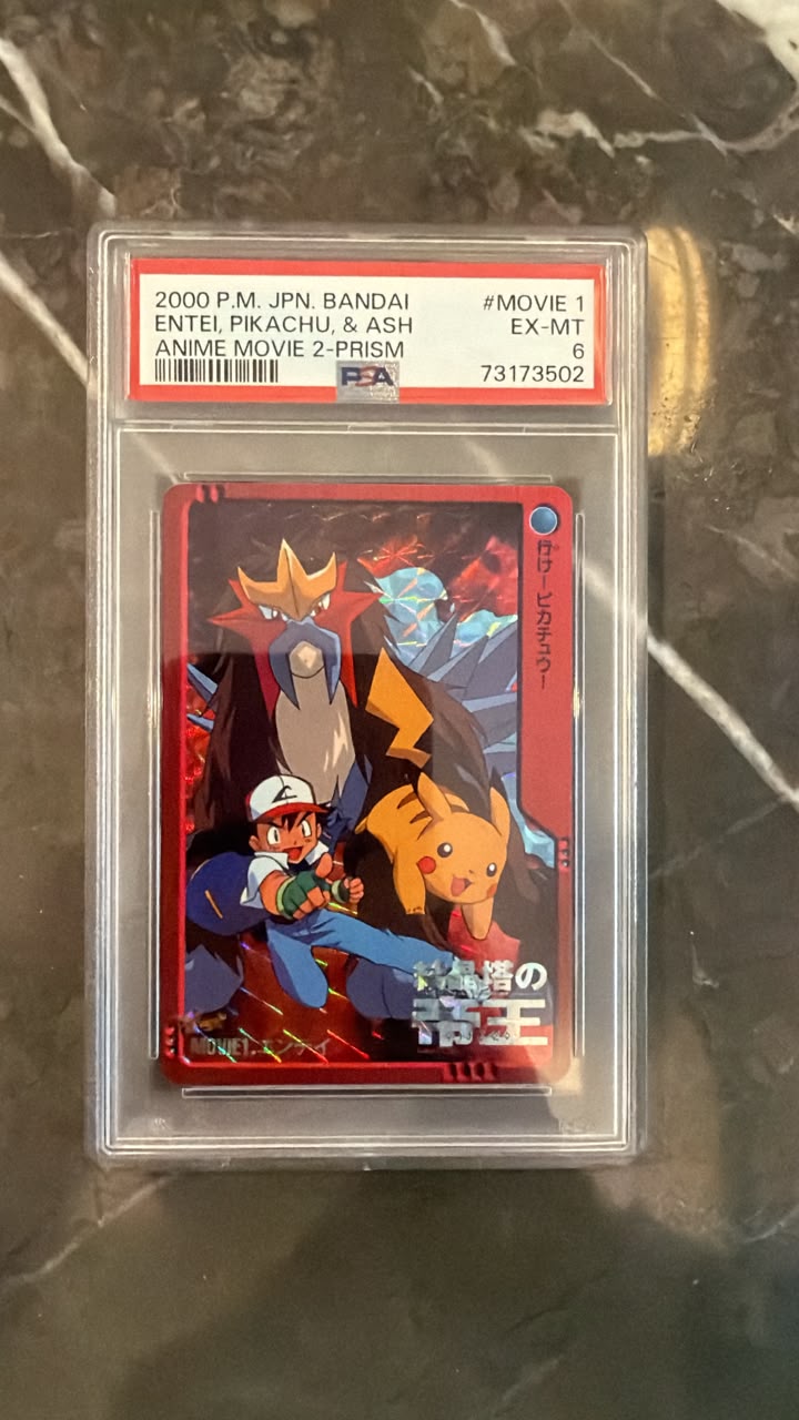 A graded Pokémon trading card featuring Entel Pikachu and Ash Ketchum, sealed in a clear PSA slab with a red label. The card is photographed on a dark marble surface.